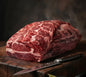 Raw beef brisket on a wooden cutting board with a knife, against a dark background