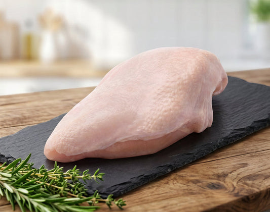 Raw chicken breast on a slate board with rosemary, set against a blurred kitchen background.
