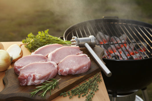 Raw pork chops on a wooden cutting board with onions and herbs in the background
