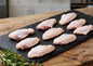 Raw chicken wings on a slate board with rosemary, set against a kitchen background.